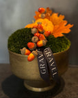 Decorative pot with autumn elements including acorns, moss, and leaves on a neutral background.