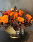 Decorative arrangement with orange flowers and pumpkins in a vase on a dark surface.