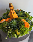Decorative arrangement with a bottle of champagne made from flowers and greenery.