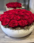 Bouquet of red roses in a white ceramic bowl on a wooden surface.