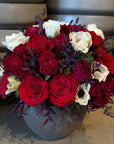 Bouquet of red and white roses in a gray vase on a textured surface.