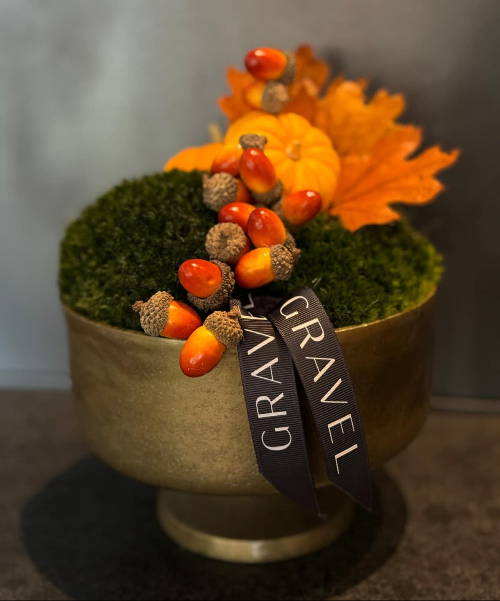 Decorative pot with autumn elements including acorns, moss, and leaves on a neutral background.