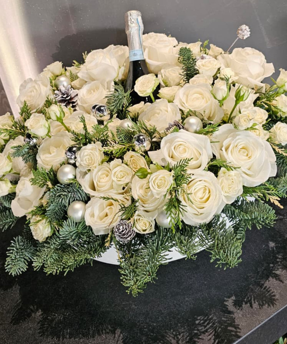Bouquet of white flowers with a bottle of champagne on a reflective surface.