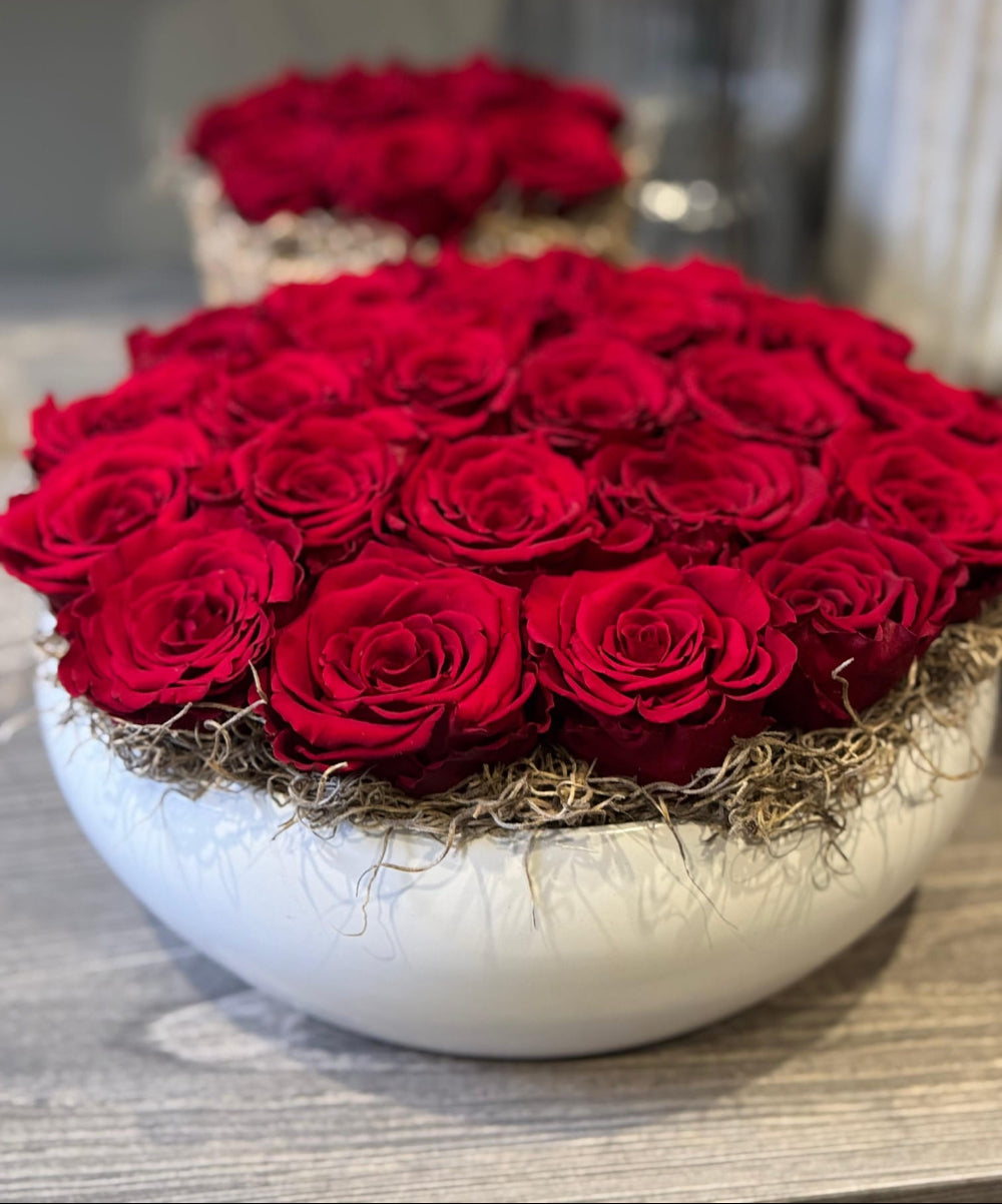Bouquet of red roses in a white ceramic bowl on a wooden surface.