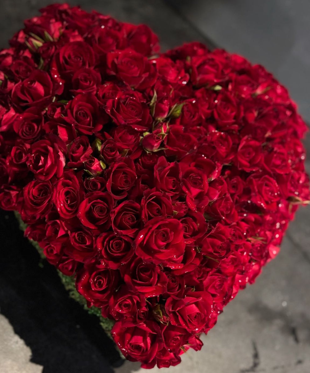 Heart-shaped arrangement of red roses on a gray surface