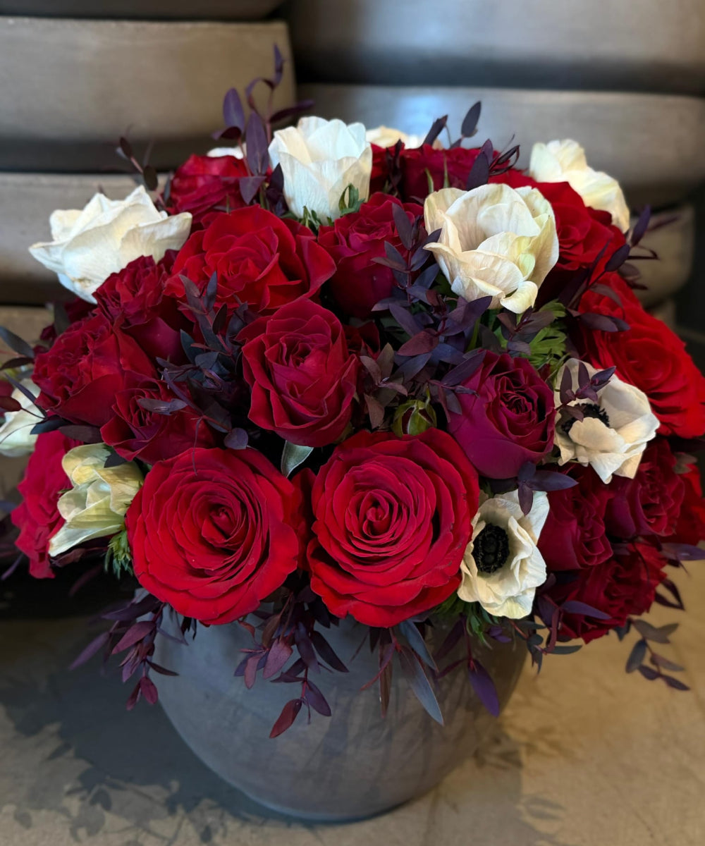 Bouquet of red and white roses in a gray vase on a textured surface.