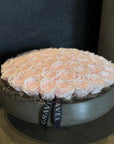 Round arrangement of peach roses in a gray box with 'GRAVEL' ribbon.