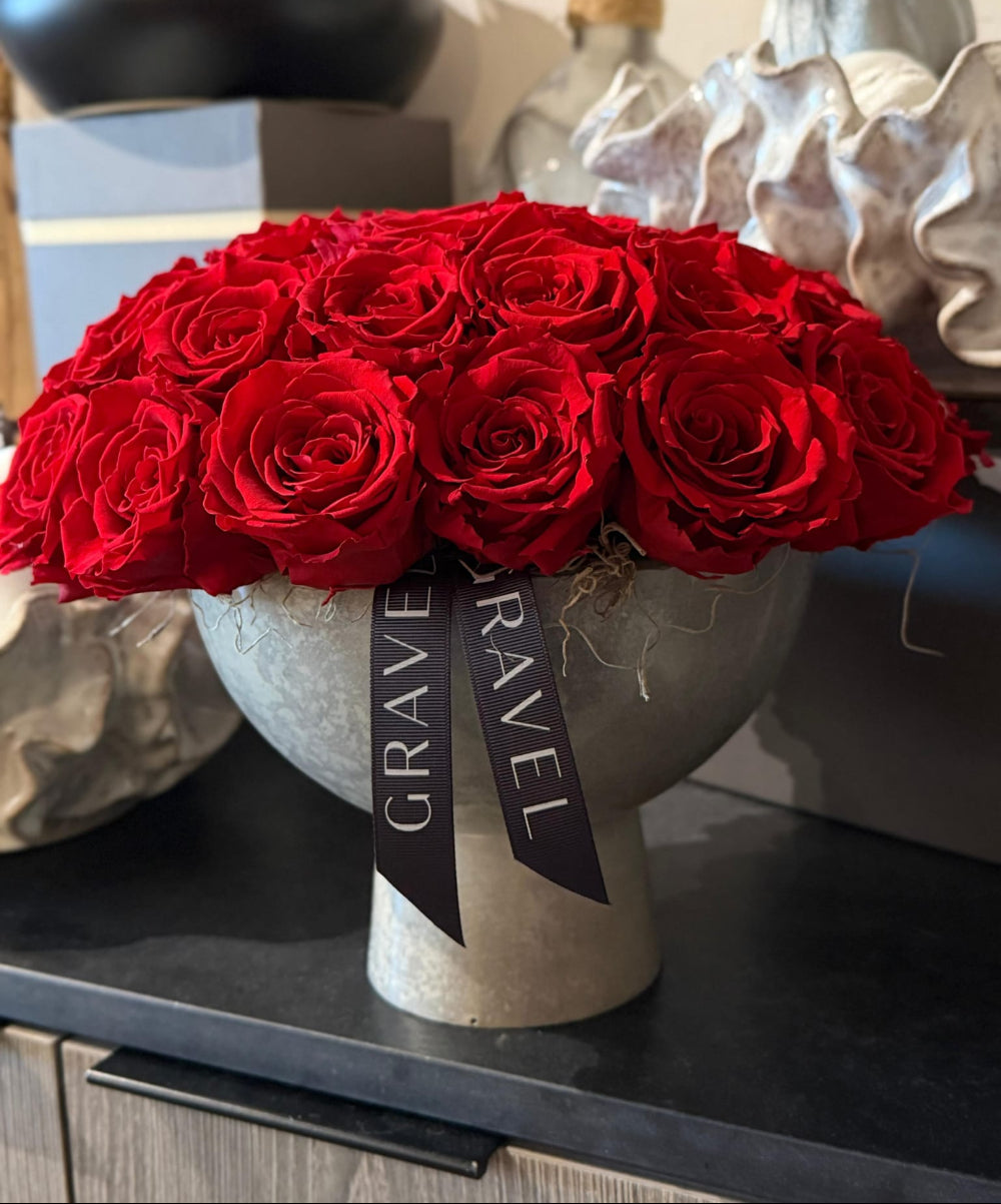 Bouquet of red roses in a decorative vase with 'GRAVE TRAVEL' ribbon on a surface.