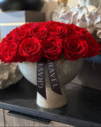 Bouquet of red roses in a decorative vase with 'GRAVE TRAVEL' ribbon on a surface.